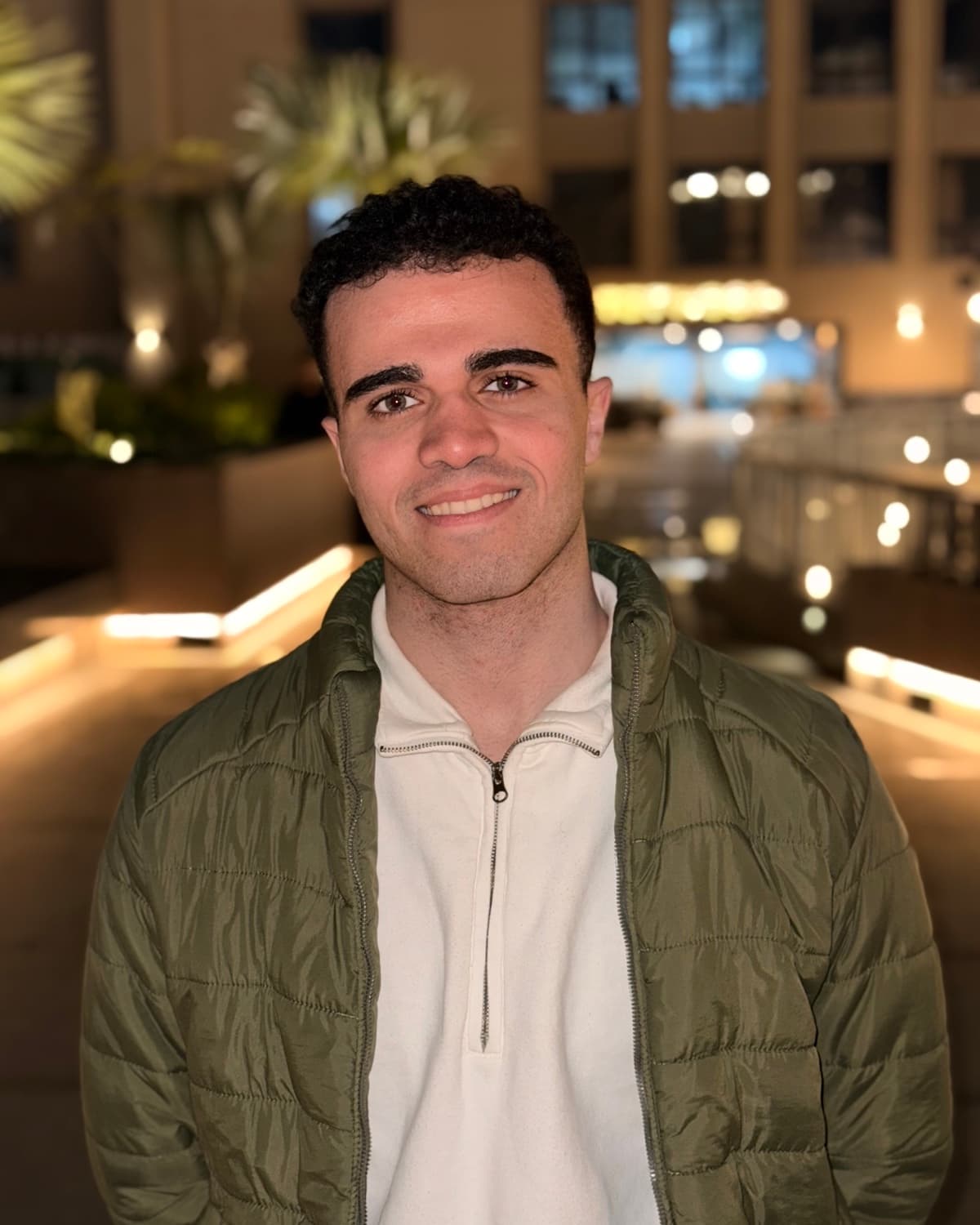 Adham Ahmed Altony at night in Cairo, warm city lights glowing behind him